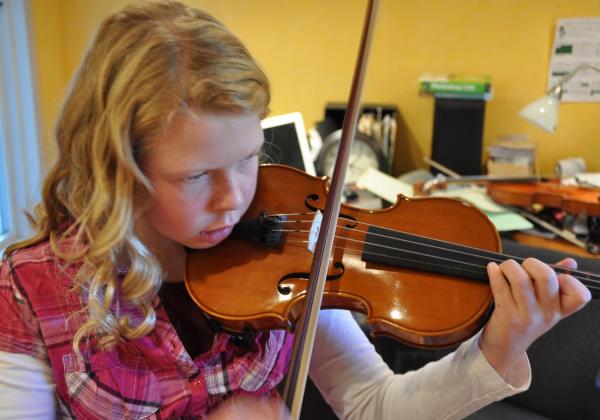 Little blonde girl intensely focused on playing violin in 3rd position