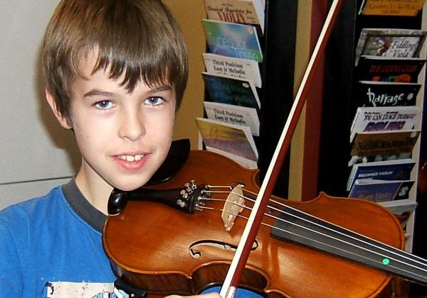 Preteen boy playing violin and smiling at the camera