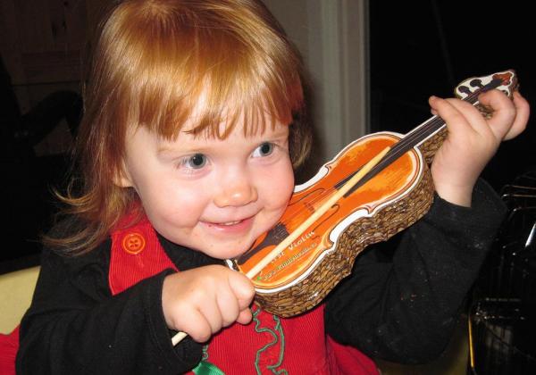 Toddler girl smiling and playing a pretend violin with a chopstick as a bow