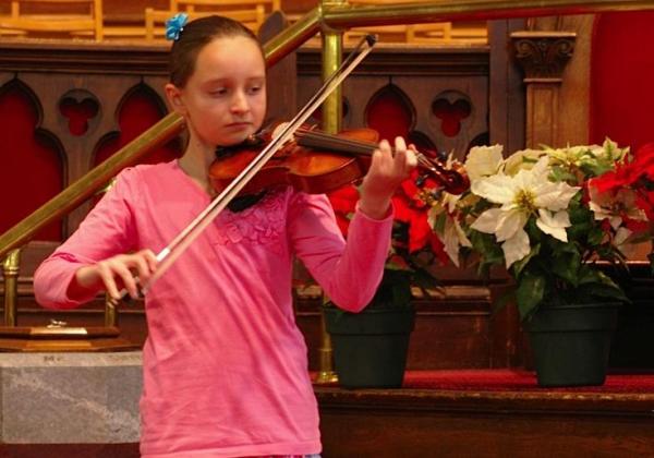 Tall girl in pink playing violin in a warmly-lit church at Christmas