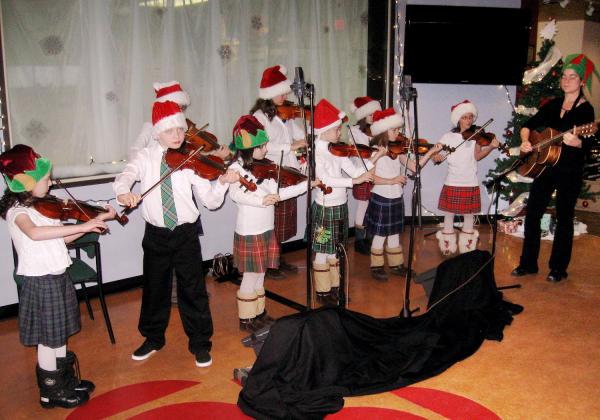 A group of many children in Santa hats playing fiddle on a stage at Christmastime