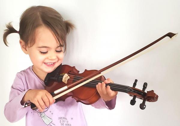 Little girl in pink shirt playing violin and smiling