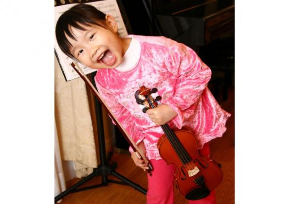 Adorable little girl in pink beaming a giggling smie as she holds her violin and bow