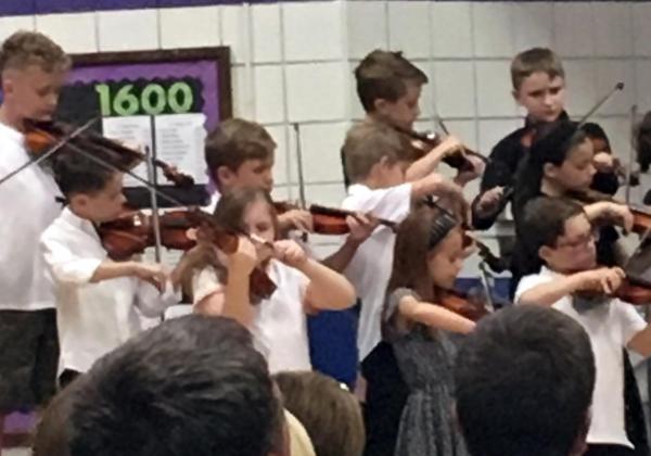 Little girl playing left-handed violin in a concert wit other kids playing right-handed
