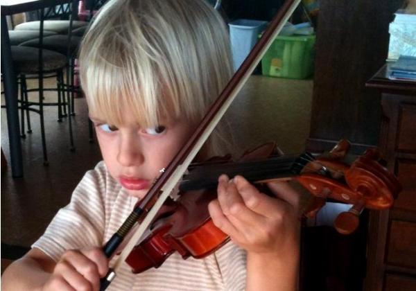 Blonde four year old boy focused on playing violin in the kitchenBlonde four year old boy focused on playing violin in the kitchen