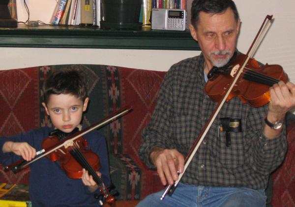 Young boy playing fiddle beside his gradnpa, who is also playing fiddle