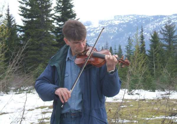 Middle-aged man playing his violin at a mountain summit with snow
