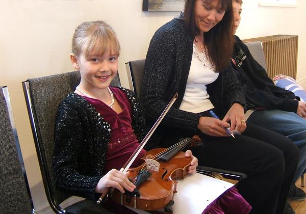 Adorable blonde girl holding a violin on her lap as her mother smiles at her