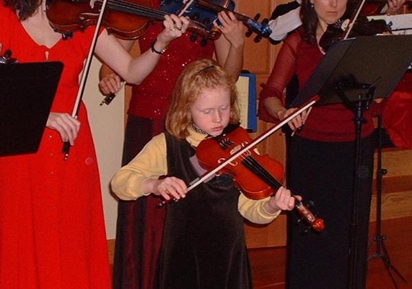 Cute little redheaded girl playing a violin with adults playing behind her