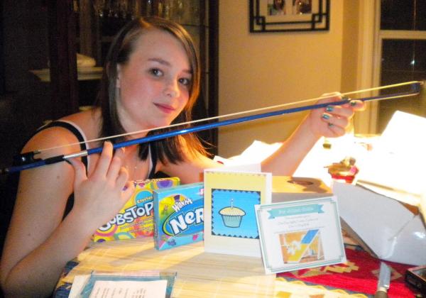 Young teen surrounded by birthday cards holds a shiny electric blue violin bow