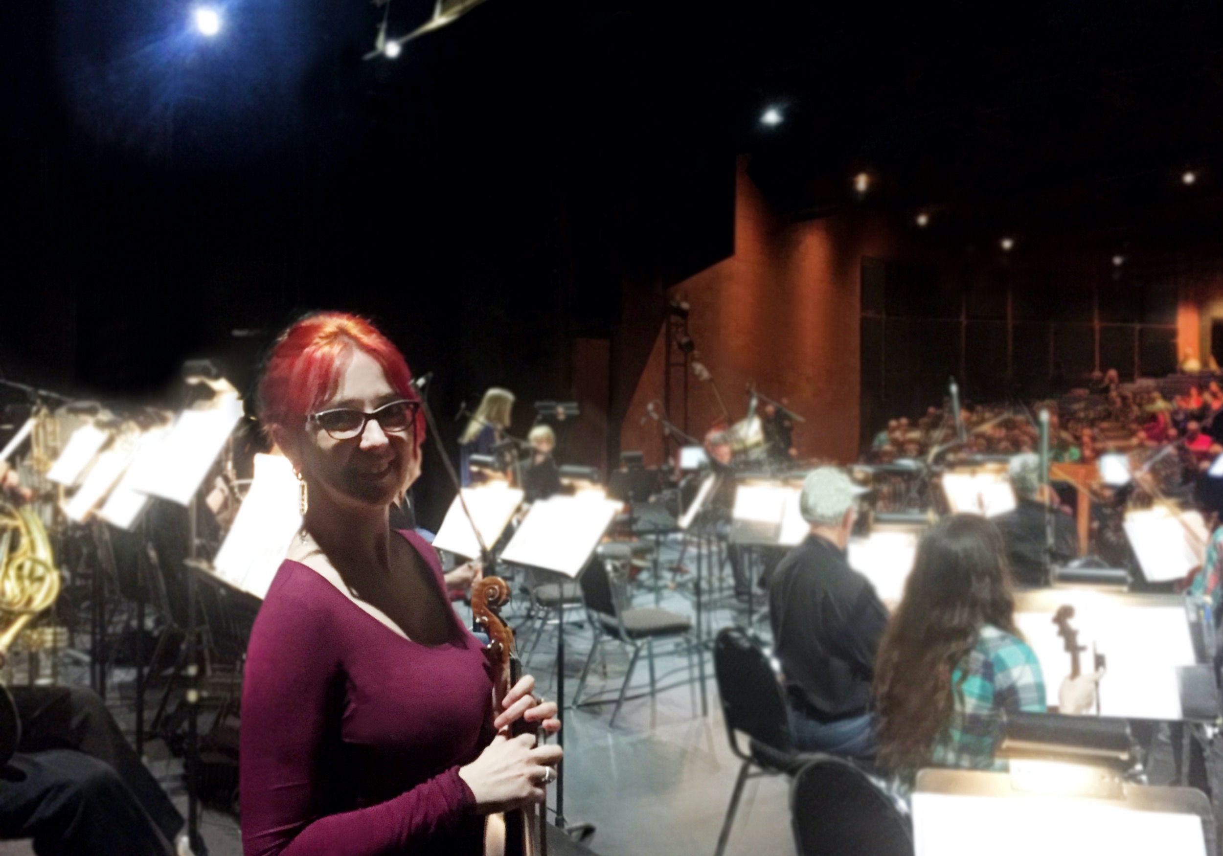 Rhiannon standing on stage with the Okanagan symphony orchestra warming up around her