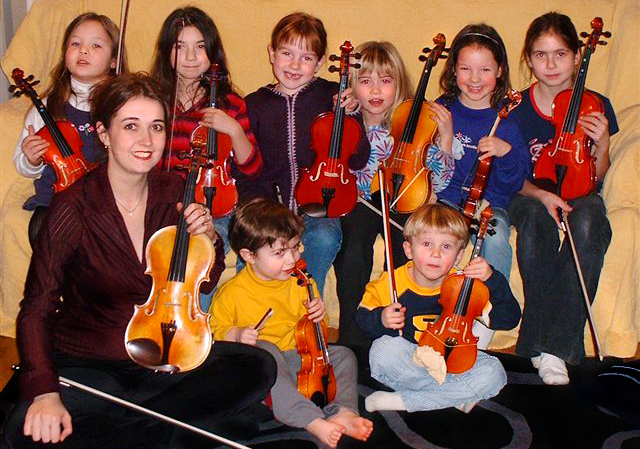 Rhiannon with several young children in a group class holding their violins
