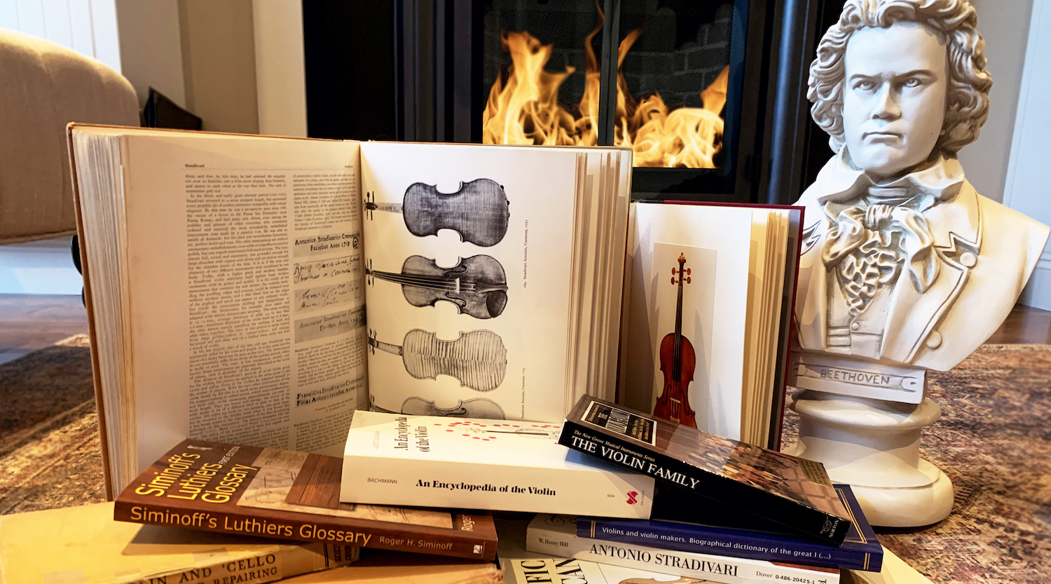 Stacks of violin encyclopedias and books with a Beethoven bust in front of a fireplace