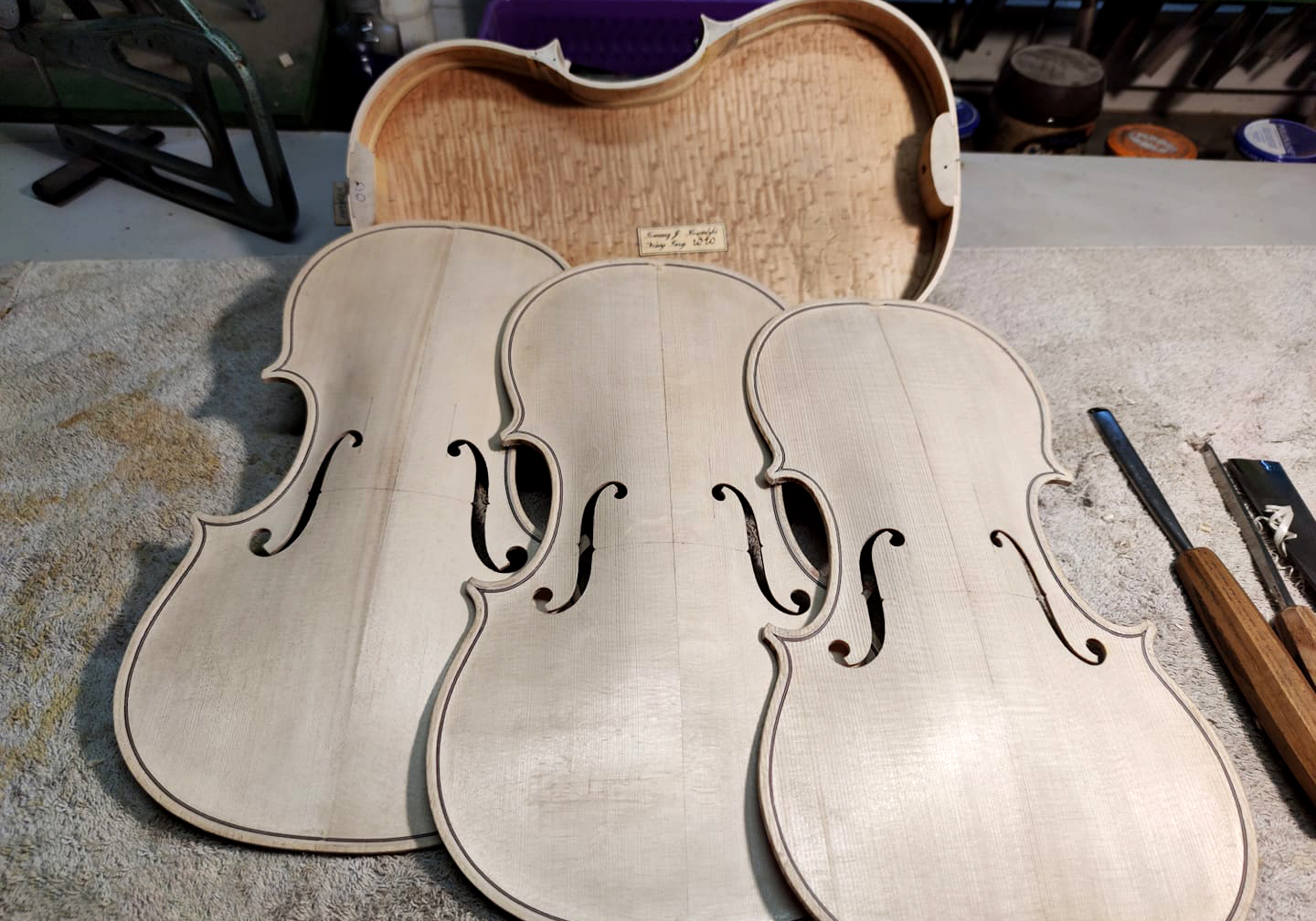 Three unfinished violin front plates on a workbench with carving tools