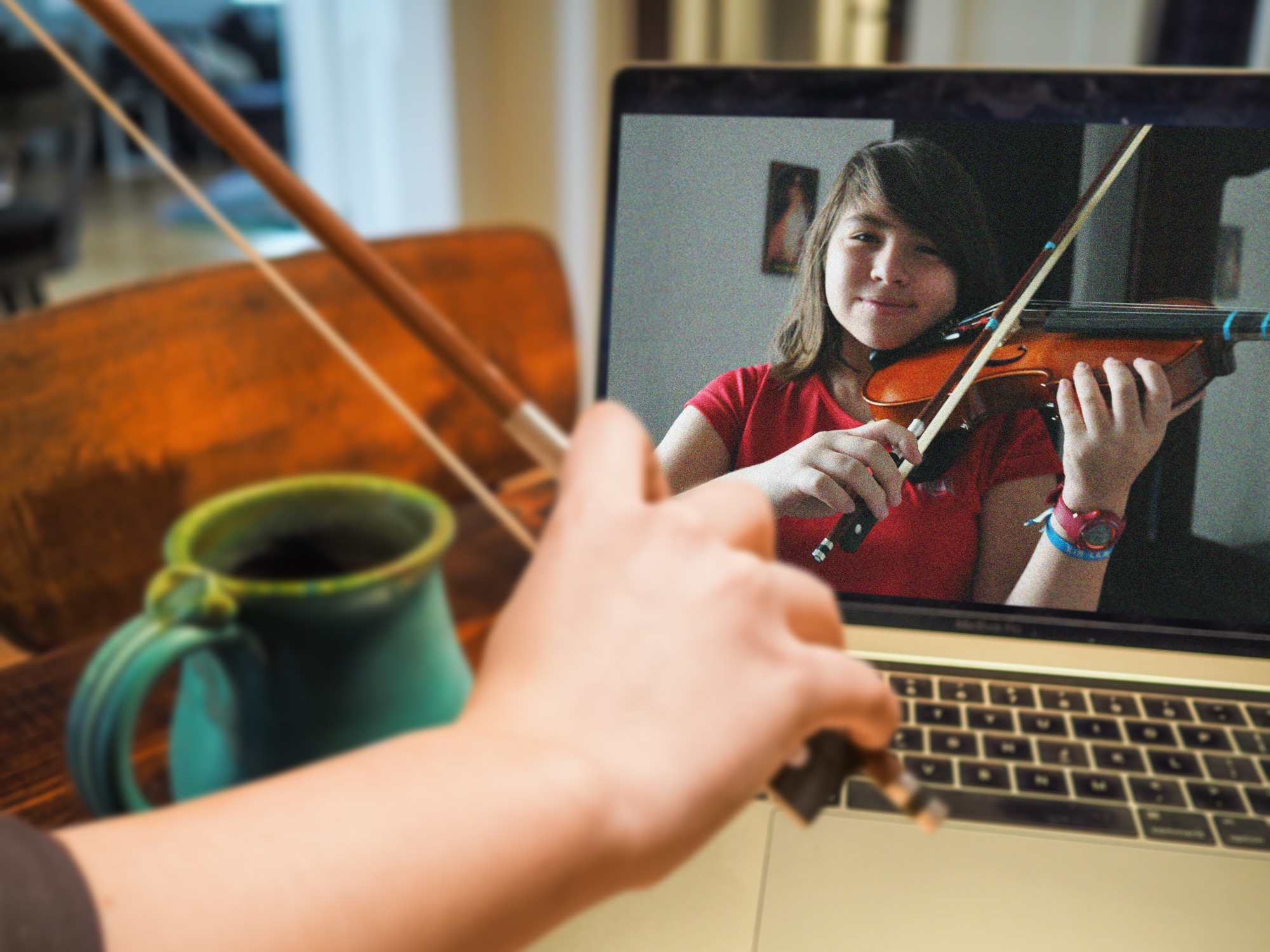 Violin teacher bow arm with laptop and young girl on the laptop screen playing violin 