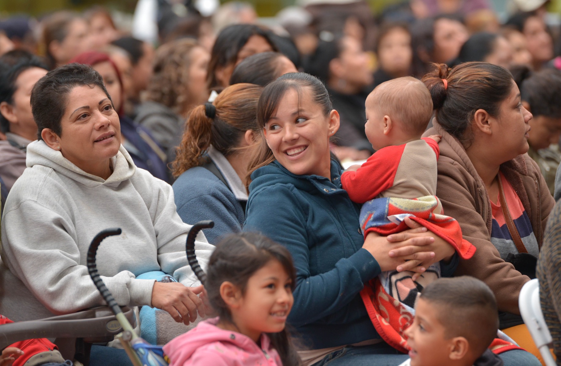 Parents and young children in an outdoor concert smiling at the performers