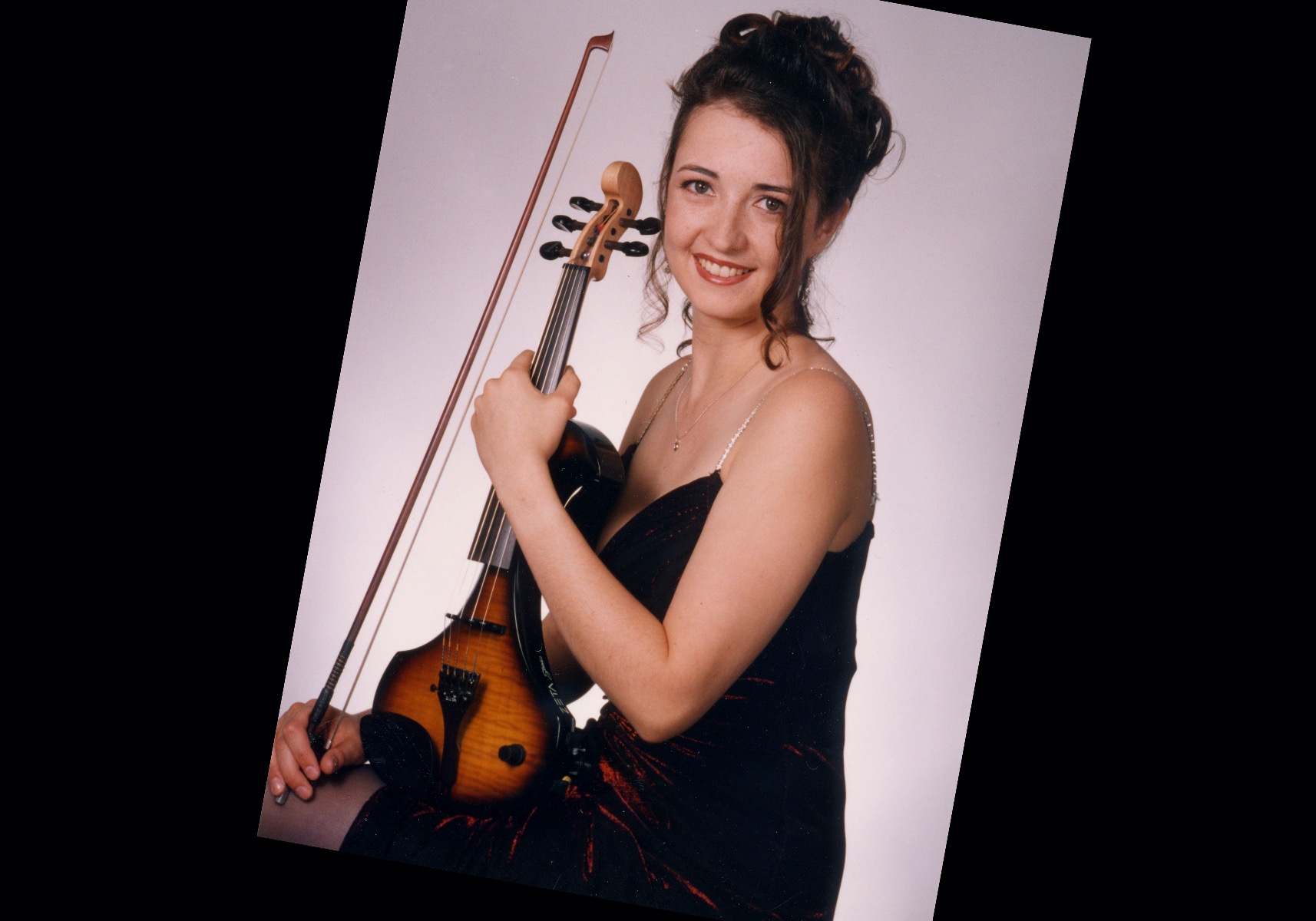 20 year old Rhiannon posed in a vintage formal dress, hair up, holding an electric violin
