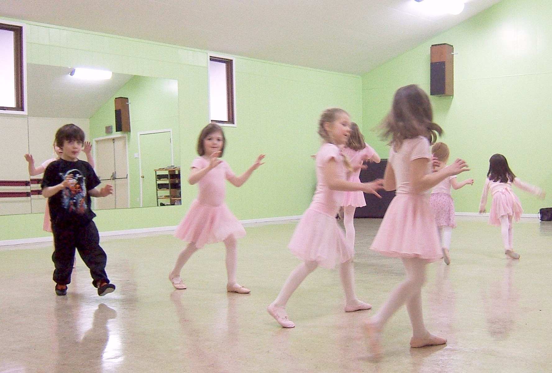 A little boy in black dances with lots of little girls in pink