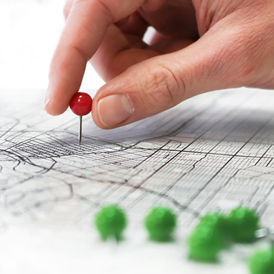 hand moving a red push pin in a map closer to a group of green pins