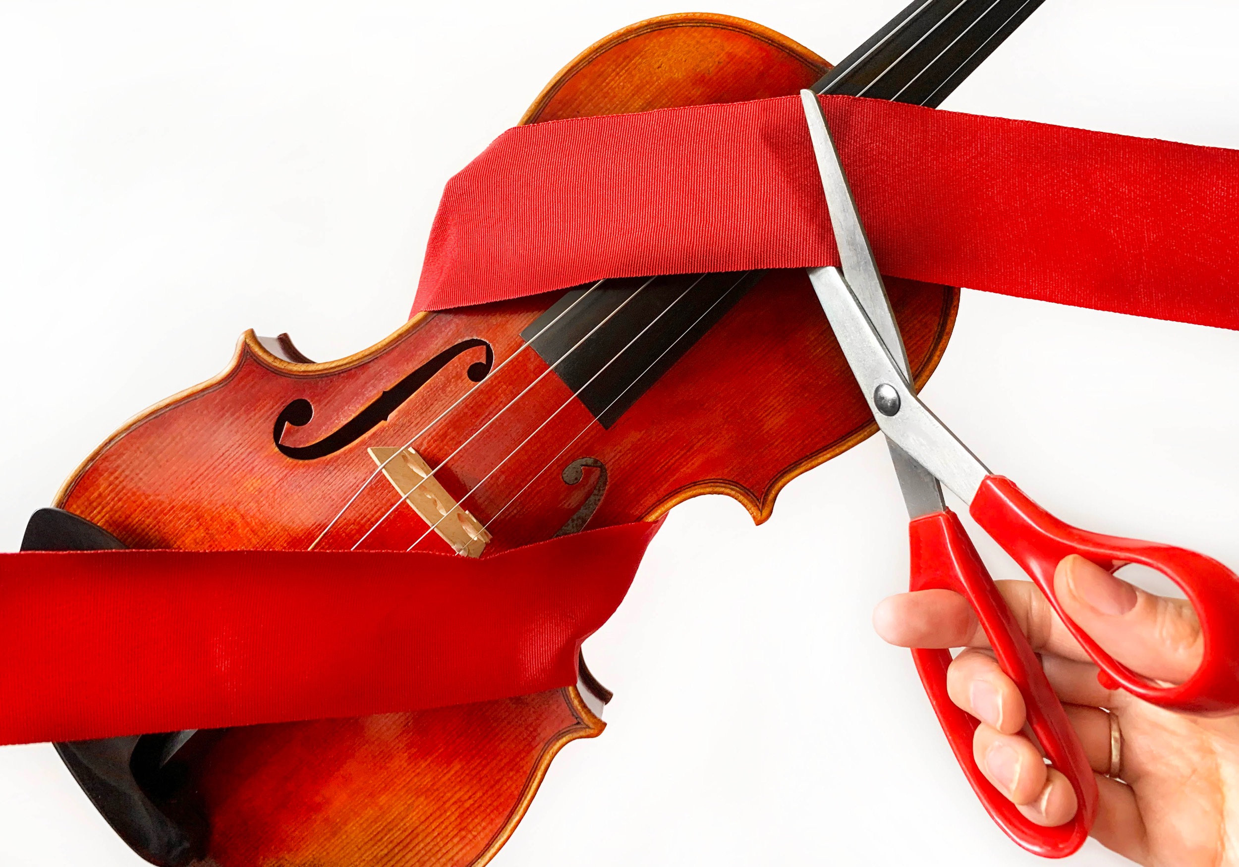 Hand with red handled scissors cutting a red ribbon wrapped around a violin