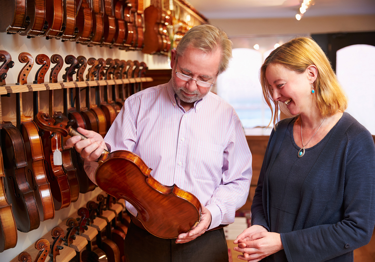 Man and woman in a violin shop holding a violin and smiling