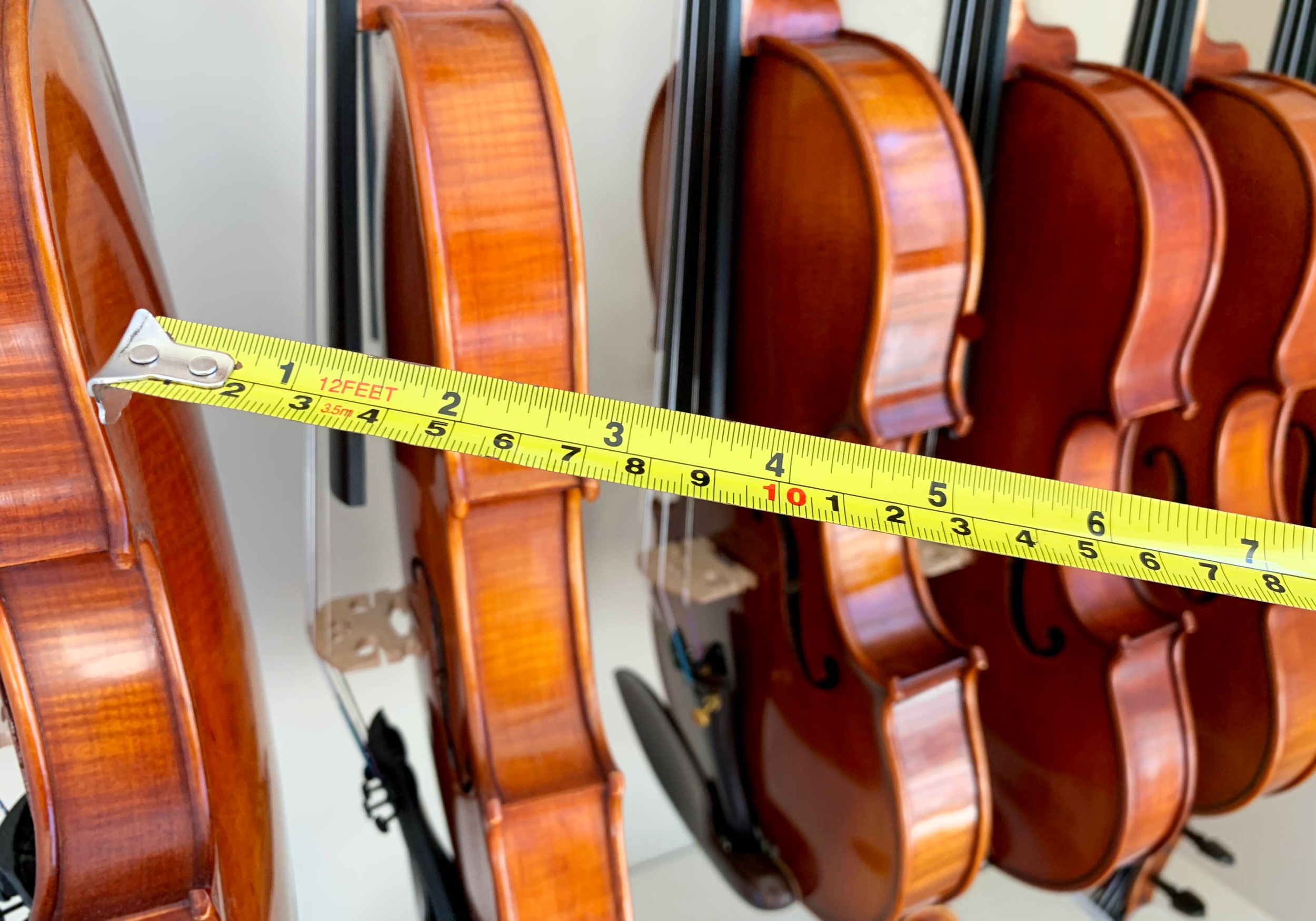Row of violins on a wall with a yellow tape measure in the foreground