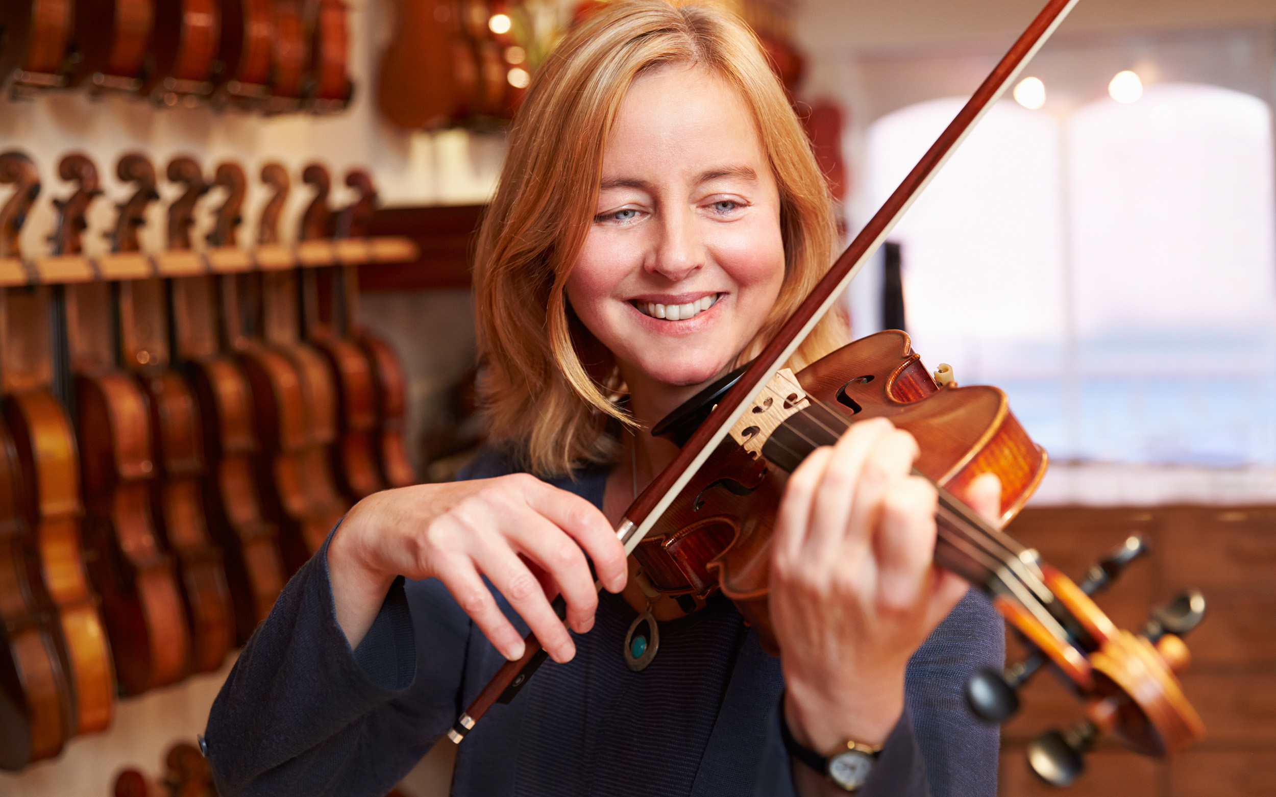strawberry blond 40-something woman smiling while playing violin with many others in the background