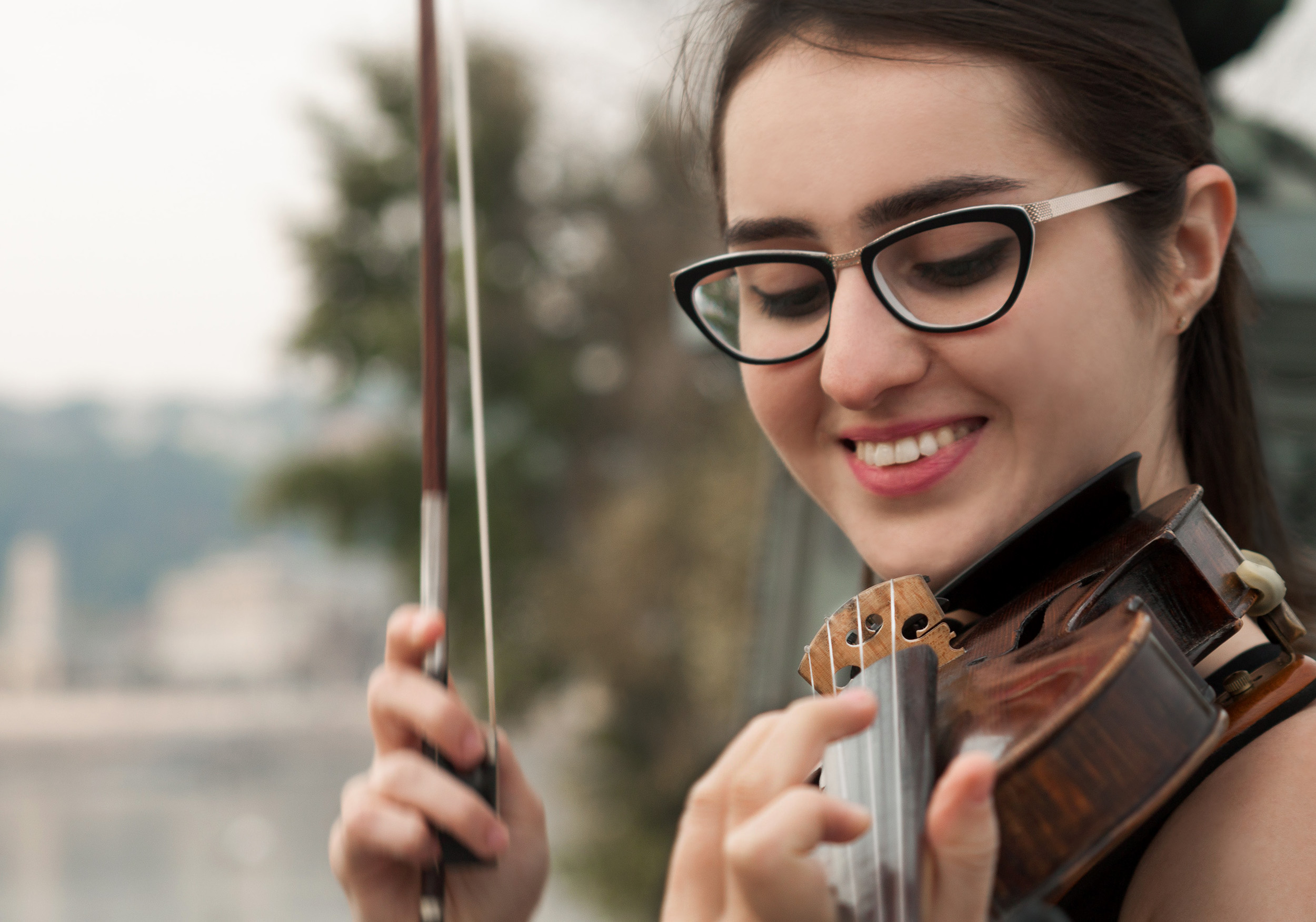 dark haired, bespectacled woman playing violin and smiling