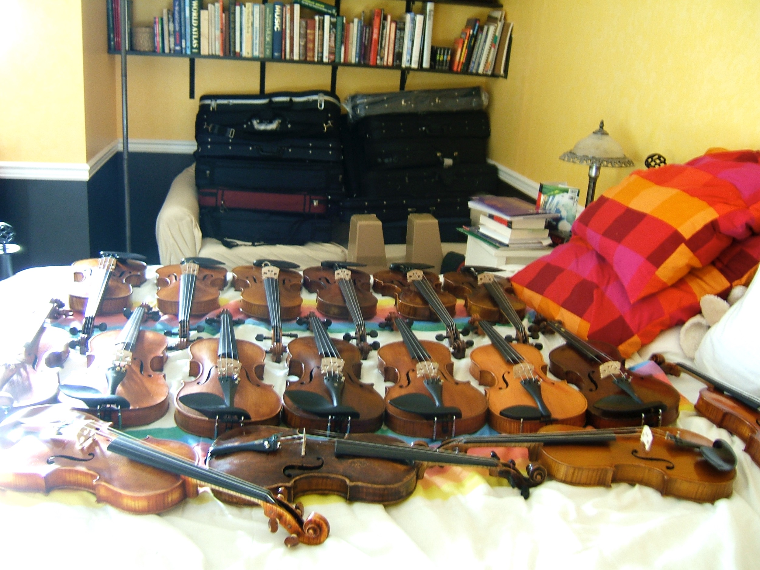 Violins and cases laid out over a bed and couch, taking up every inch of space