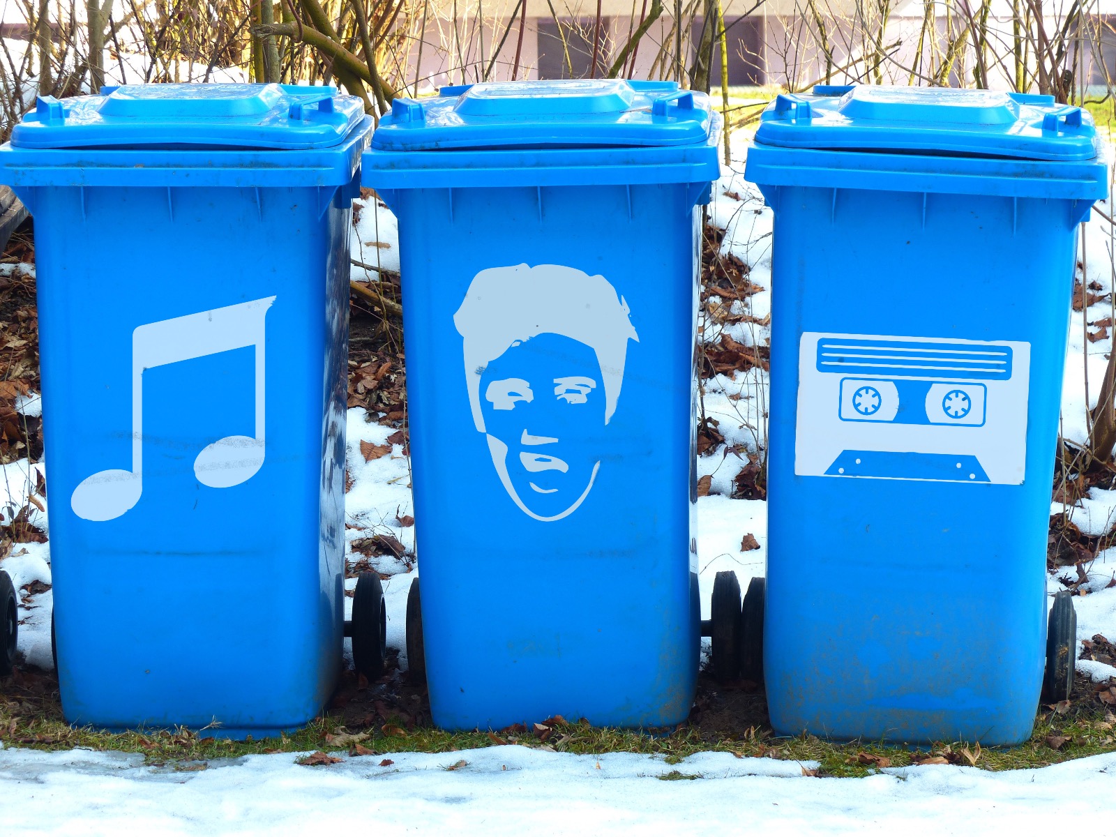 Giant blue bins on a roadside that have decals of music notes, Elvis' face and a cassette tape