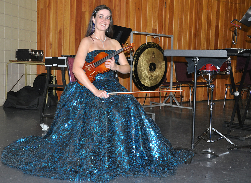 Rhiannon wearing a sequinned teal ballgown and holding a handmade Zhu violin on the symphony stage