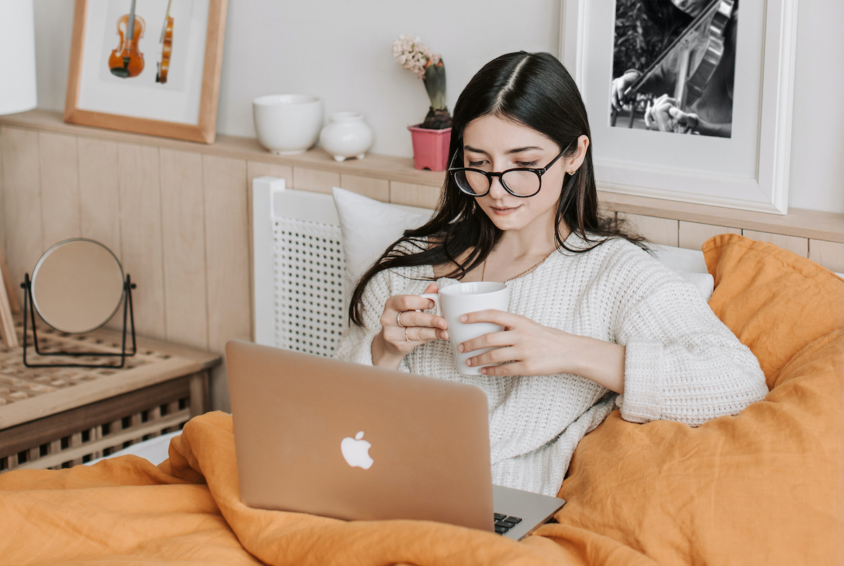 woman sitting up in bed with a coffee cup and her laptop