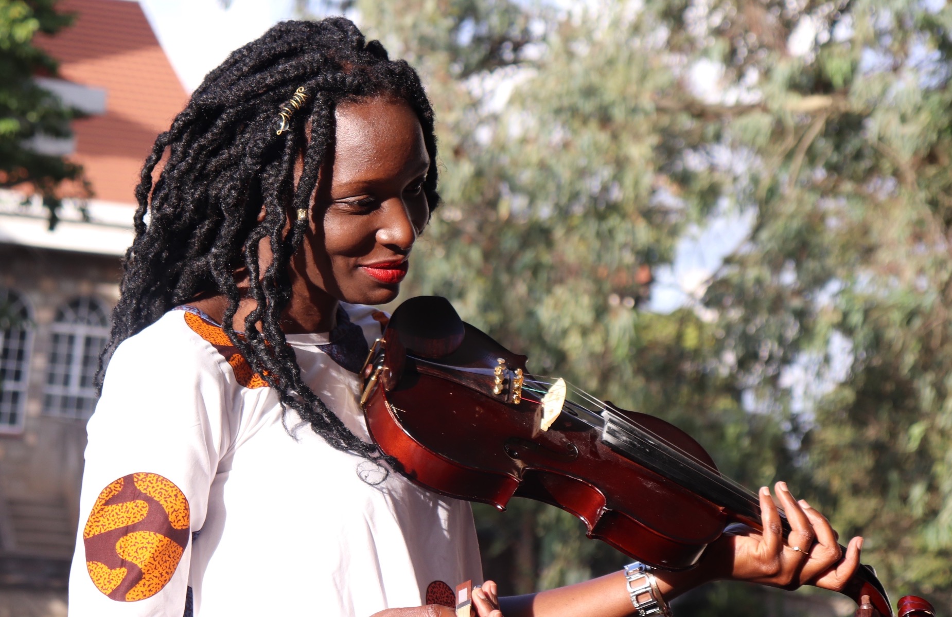 Woman with cornrow braids holding violin just under her chin and smiling