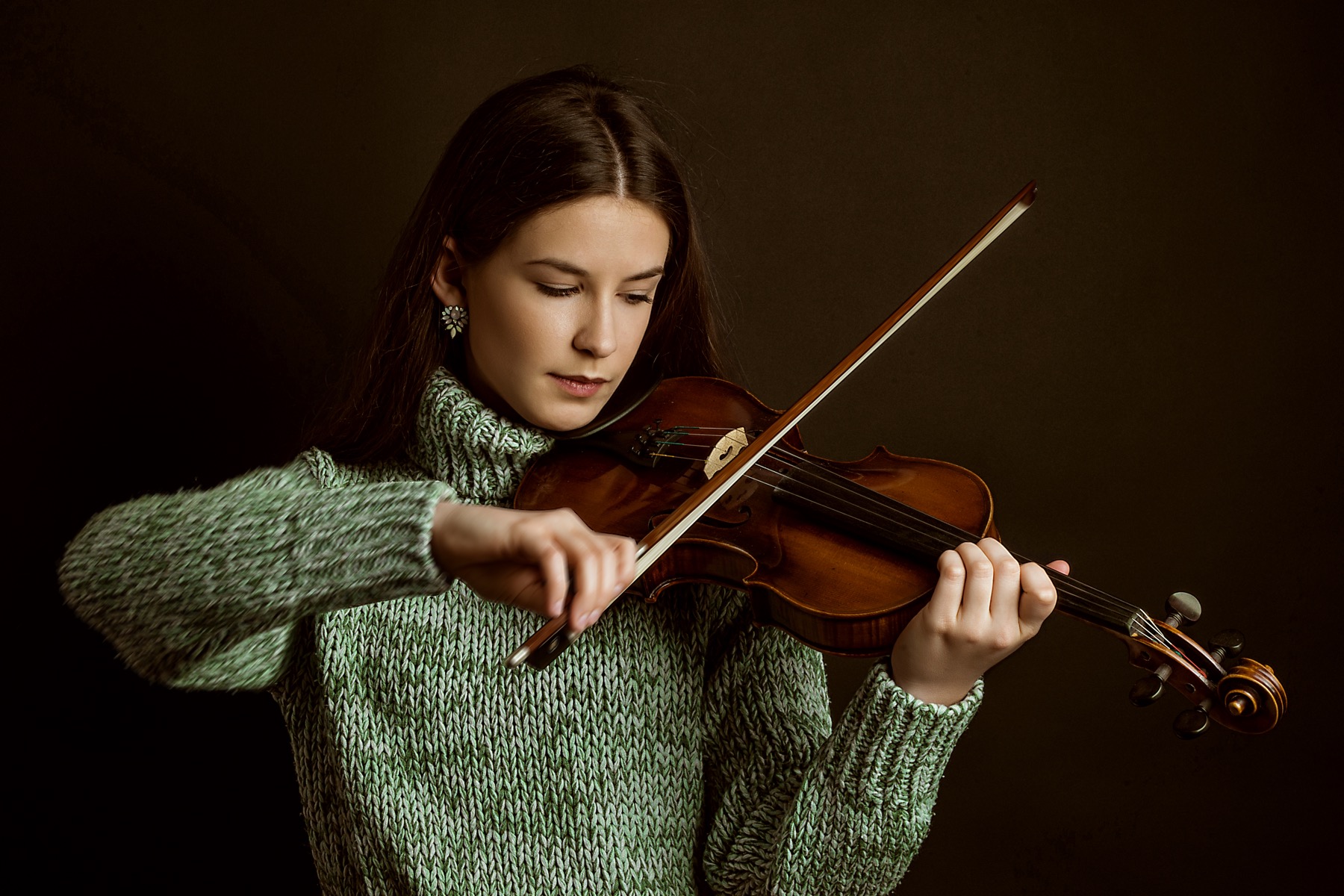 Young woman in green sweater playing violin with bow arm moving