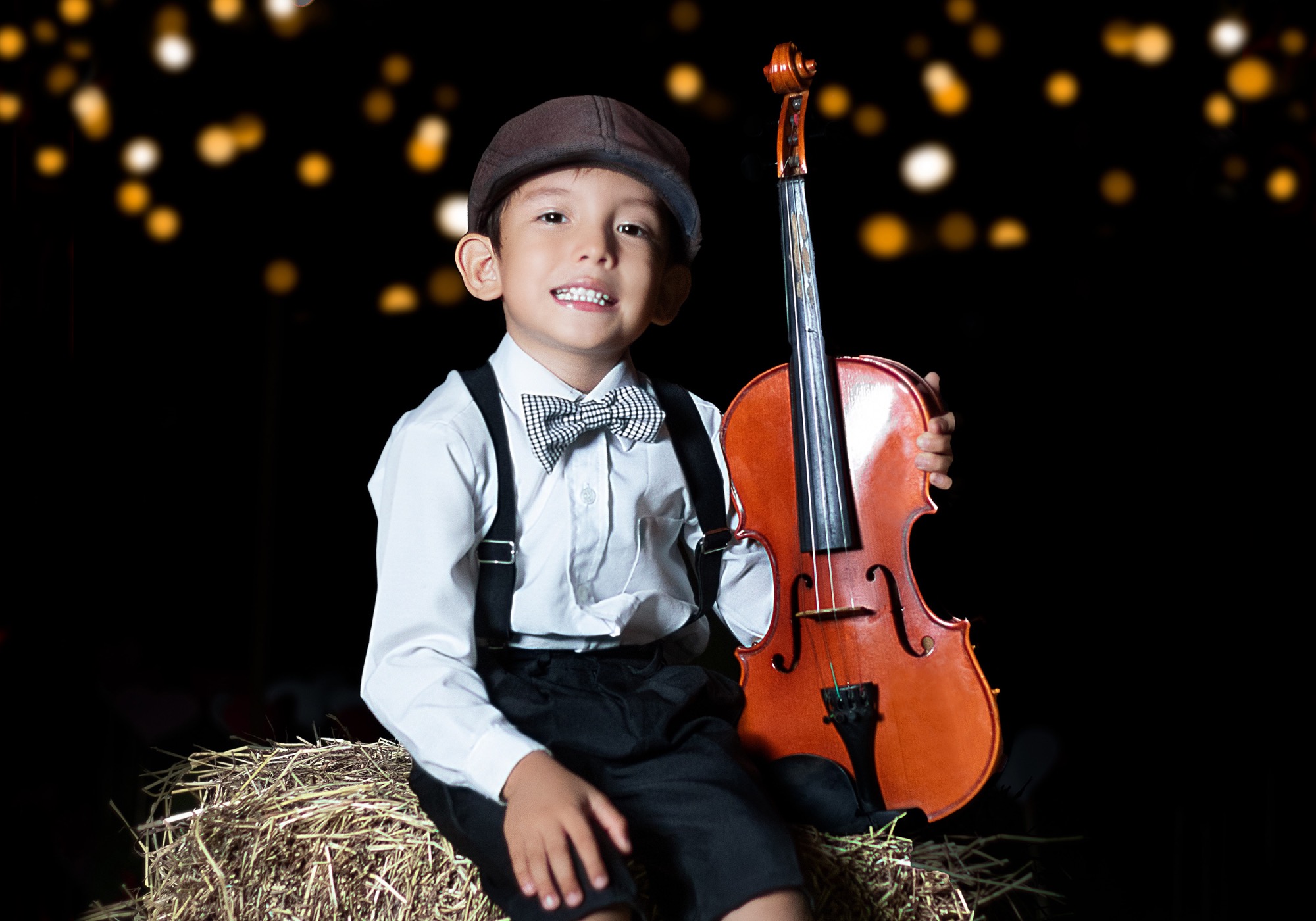 little boy sitting on a hay bale holding an oversized violin