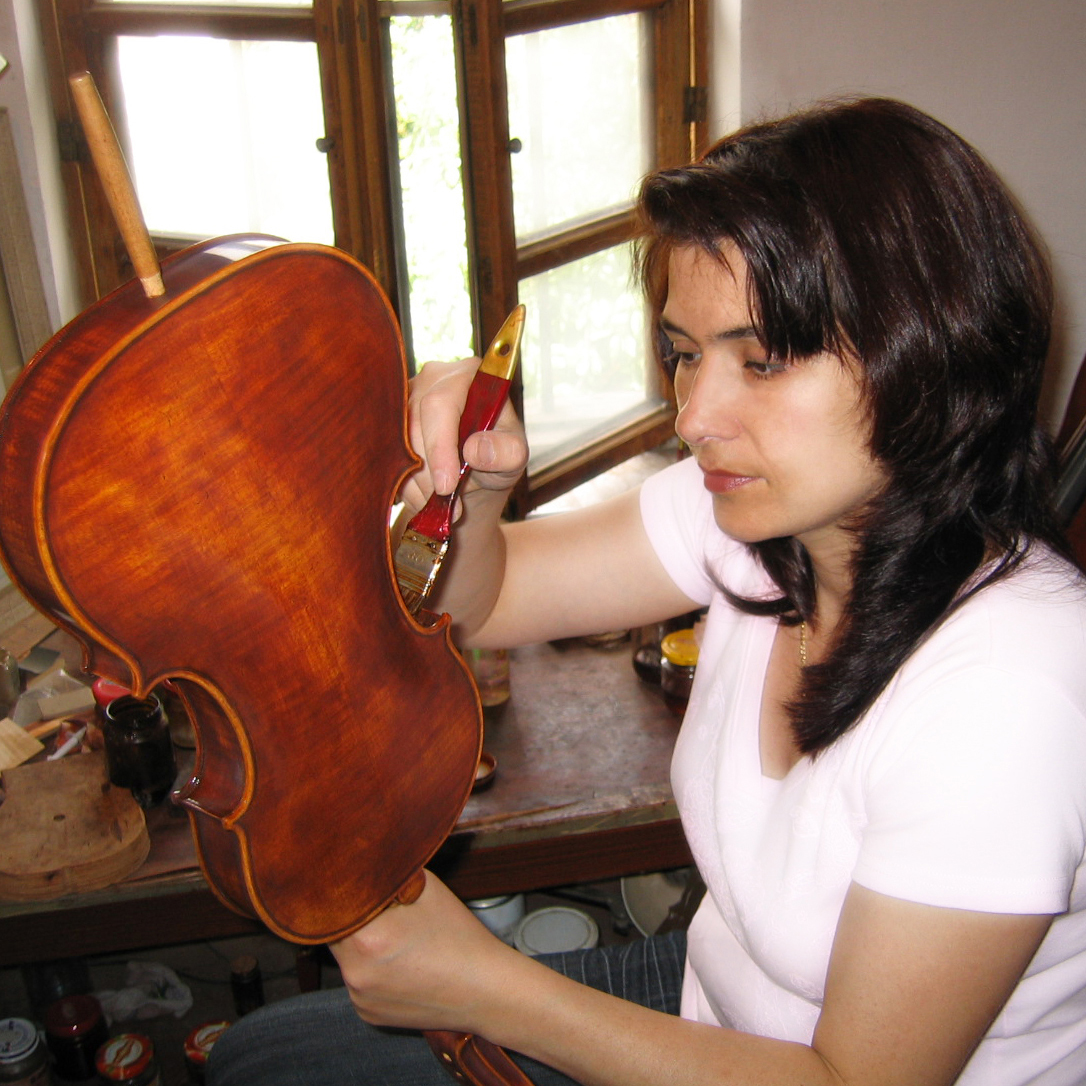 Angela Moneff varnishing a violin with a brush in her home workshop