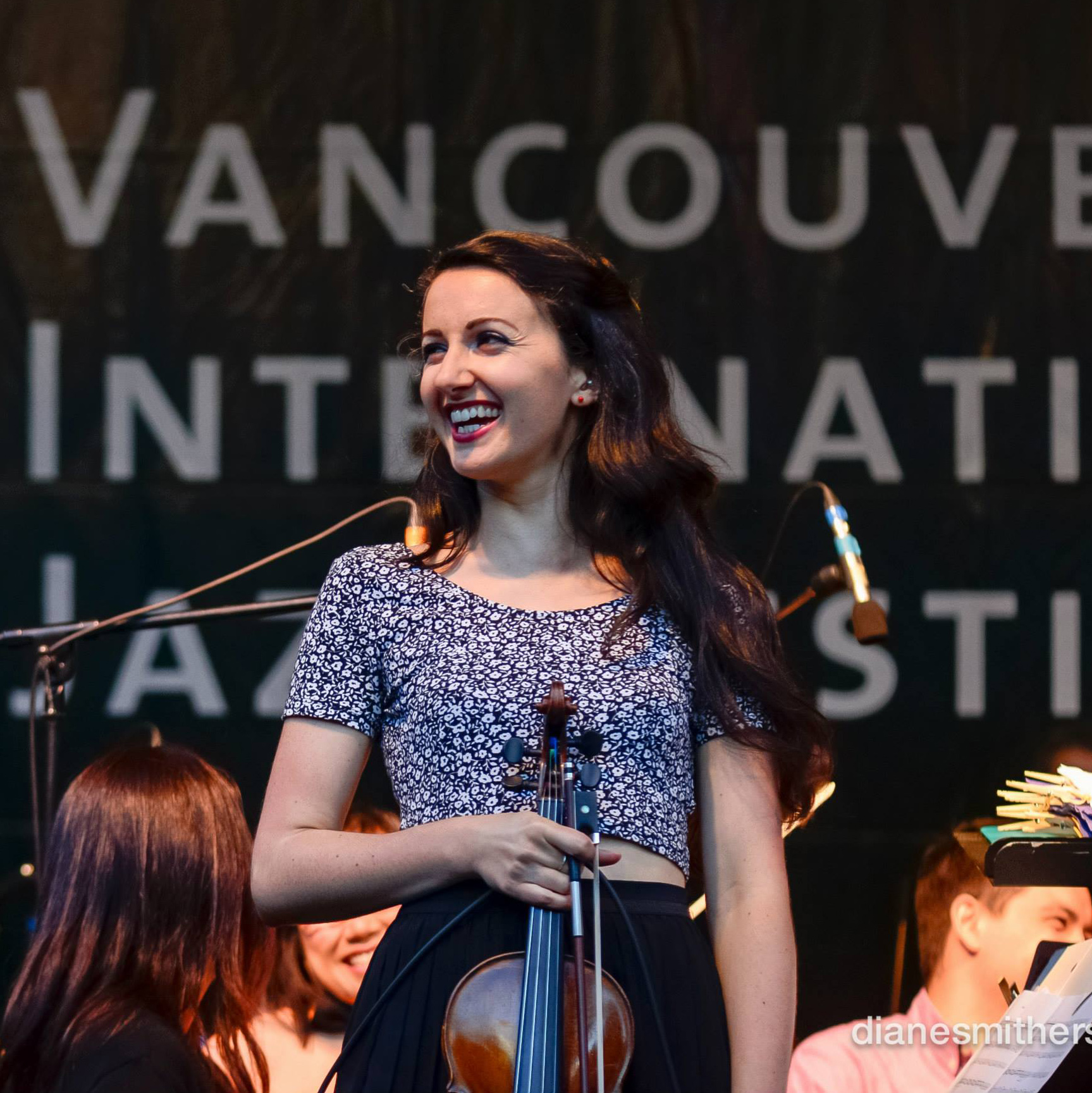 Elyse holding her violin and smiling on the stage of the Vancouver Jazz Festival