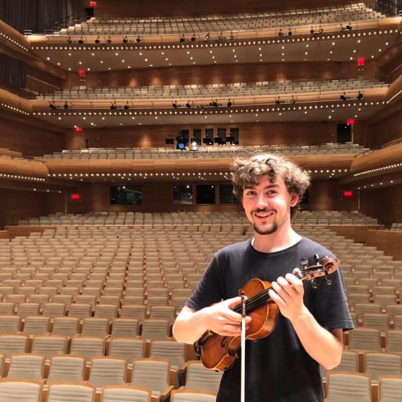 James holding his violin in a large concert hall